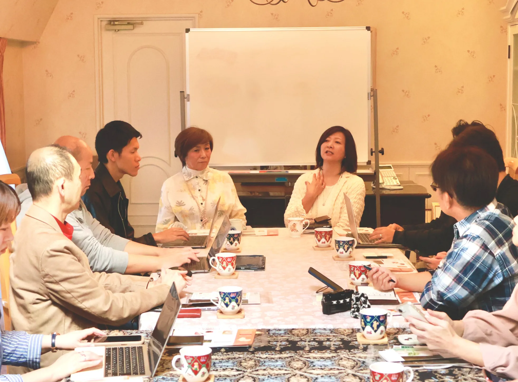 会議室で参加者がテーブルを囲み、ノートPCや資料を使って意見交換している様子。